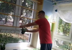 Na zdjęciu widać rodzica, który pomaga przy tworzeniu ziołowego okna.